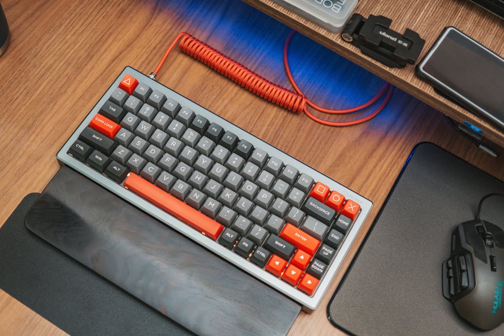 Modern mechanical keyboard with red accents on wooden desk, captured from above.