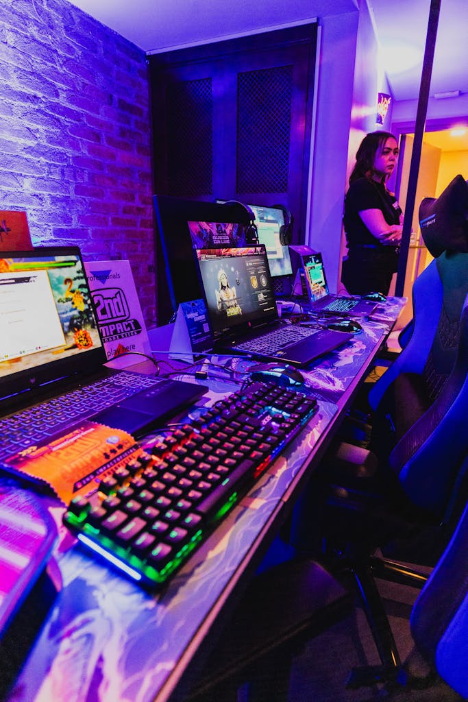 Vibrant gaming setup with RGB keyboards and laptops at a trade show, featuring a woman in the background.