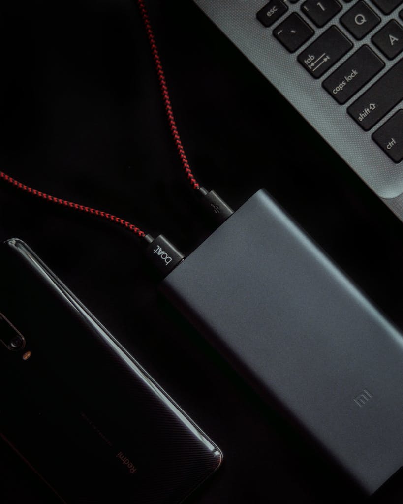 A close-up shot showcasing a laptop, smartphone, and power bank connected by cables, highlighting tech connectivity.