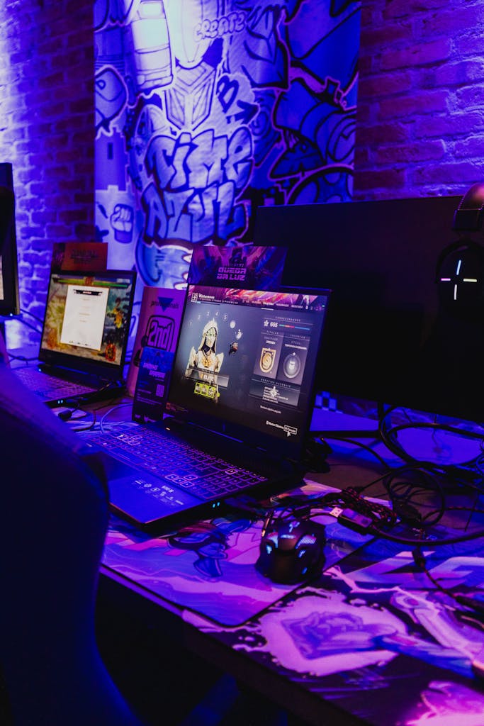 A dynamic gaming station with laptops and accessories under vibrant purple lighting, capturing the essence of contemporary gaming technology.