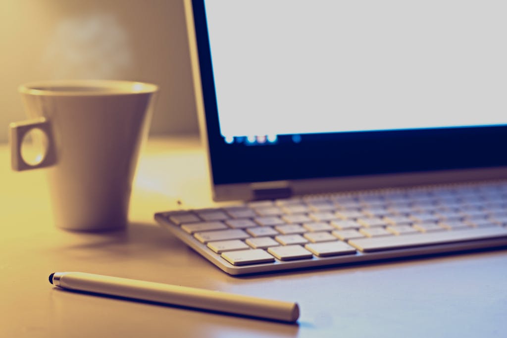 Cozy office setup with a laptop, keyboard, pen, and coffee cup on a desk.