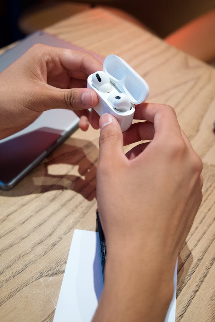 Person holding a pair of wireless earbuds in a case on a wooden table.