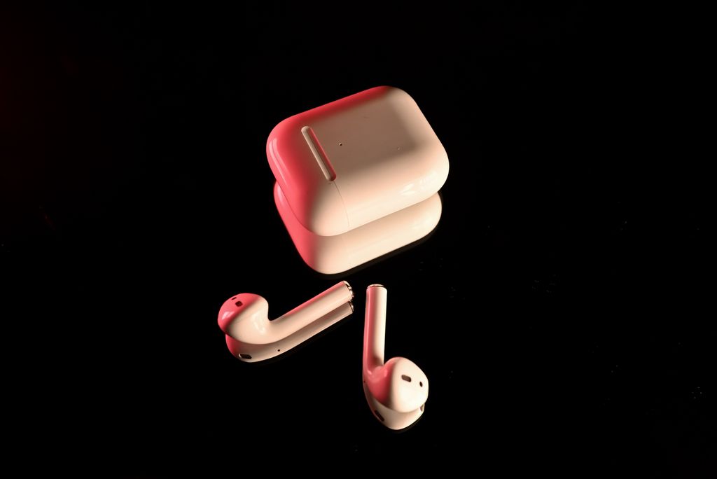 White wireless earbuds with a charging case, highlighted with red lighting on a reflective black surface.